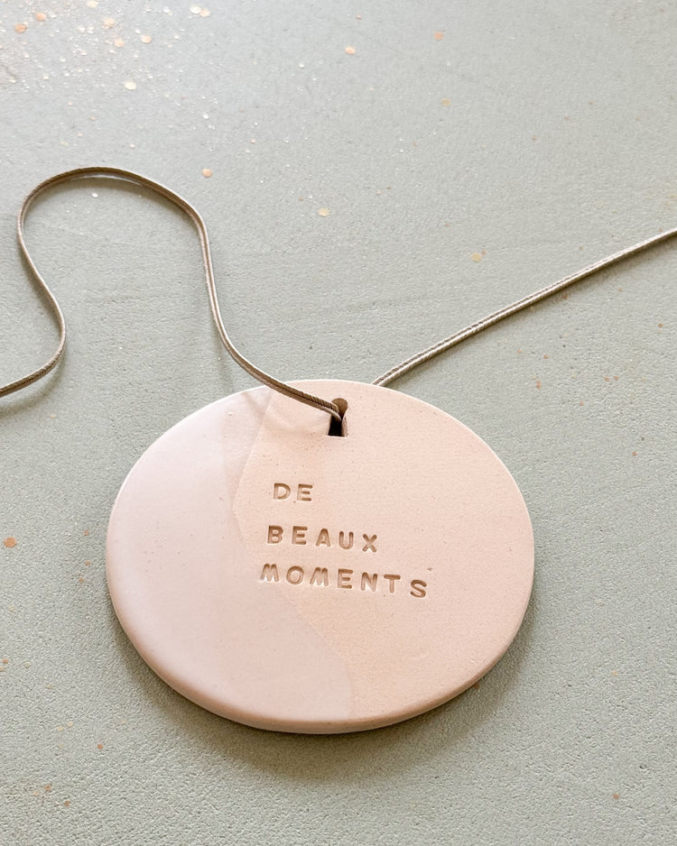 Le mantra en céramique Domaine Singulier  gravé des mots "de beaux moments". Un objet décoratif à poser ou à suspendre, à parfumer avec son cordon 100% en soie. A offrir et à s'offrir.